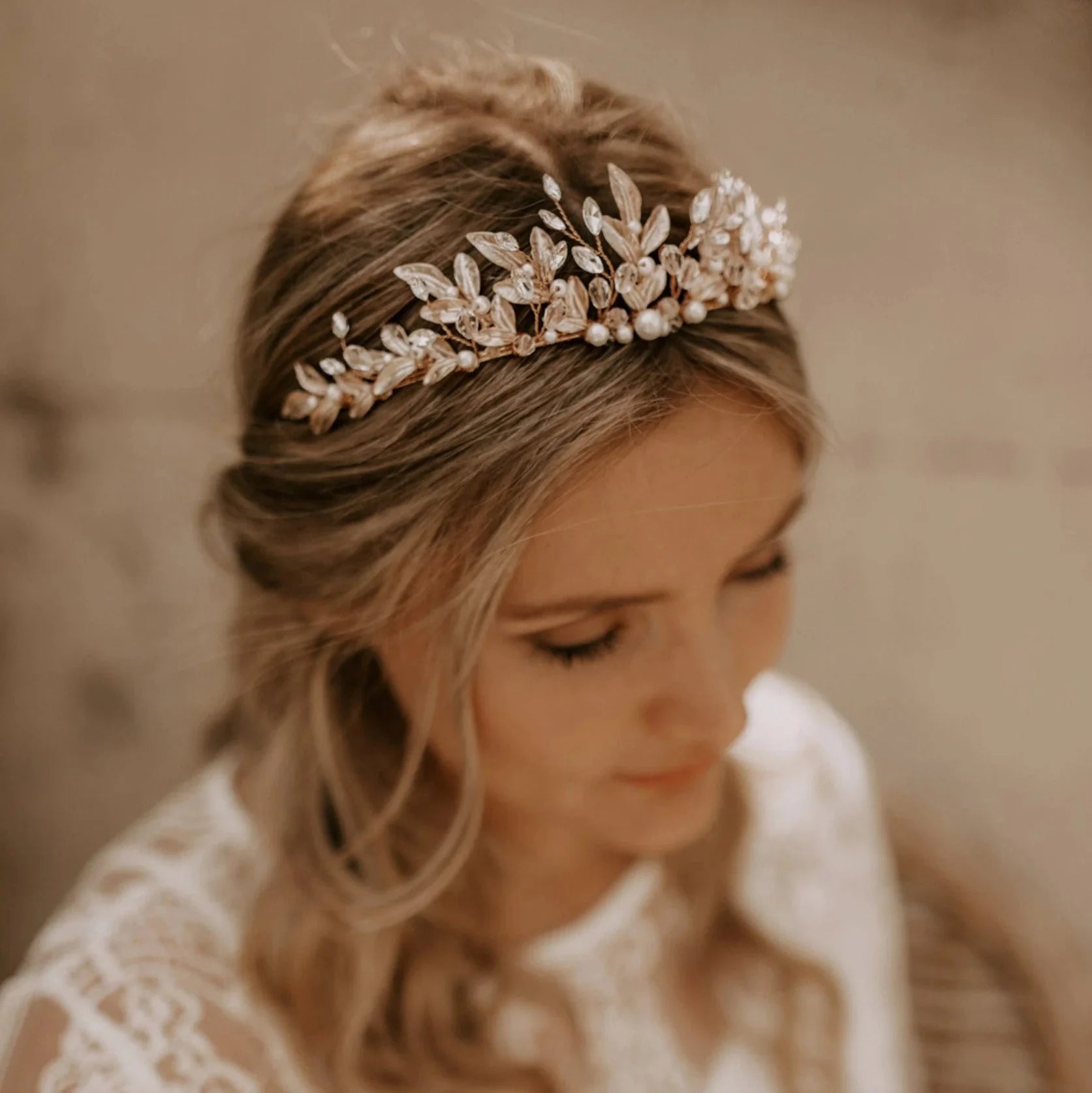 Eine Braut in einem langärmeligen Spitzenkleid und Kopfschmuck wird von einem Bräutigam in einem weißen Hemd umarmt und am Hals geküsst, während sie auf einer Sandfläche mit Bäumen im Hintergrund steht.